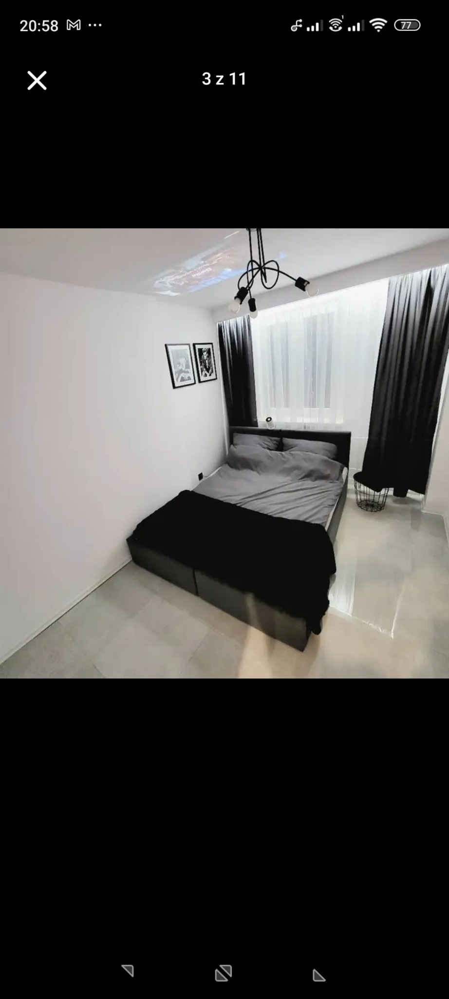 Minimalistyczna sypialnia w odcieniach szarości i czerni. Na suficie widoczny projektor. Dwa czarno-białe portrety na ścianie. Nowoczesny design wnętrza.