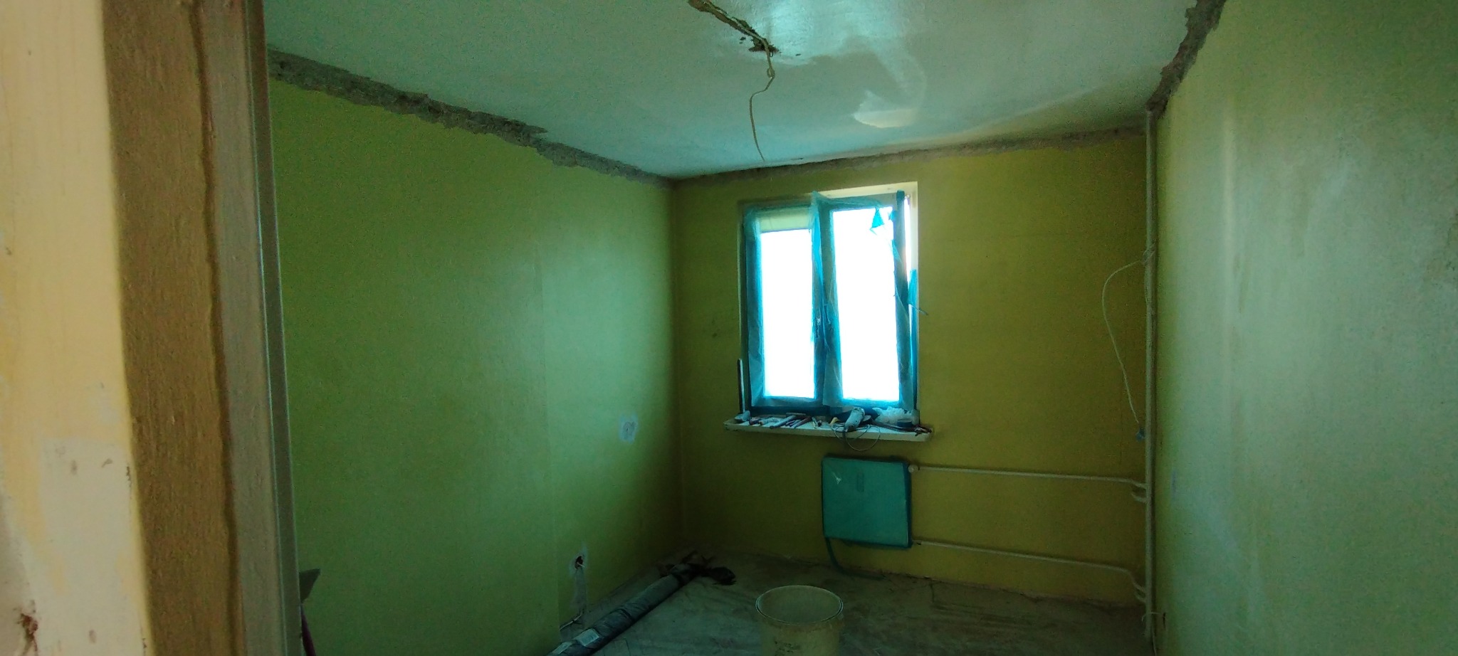 Pokój w trakcie remontu: świeżo pomalowane na zielono ściany, okno zabezpieczone folią, widoczne ślady po pracach na suficie, narzędzia na parapecie.
