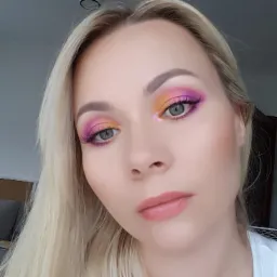 Portret blondwłosej kobiety z profesjonalnie wykonanym, kolorowym make-upem oczu w odcieniach różu, fioletu i żółci, wykonanym w Wieliczce, z widocznymi sztucznymi rzęsami i delikatnym makijażem ust.