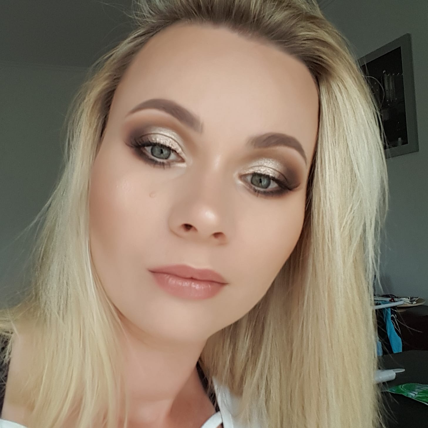 Portret kobiety z blond włosami i profesjonalnie wykonanym, błyszczącym makijażem oczu w odcieniach złota i brązu oraz delikatnym podkreśleniem ust błyszczykiem.