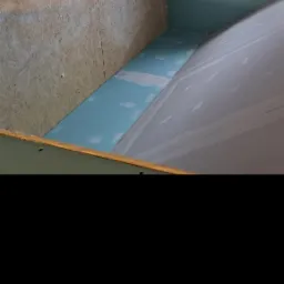 Skośna ściana z płyt karton-gips, częściowo wyszpachlowana, z widoczną drabiną i oknem. Etap prac wykończeniowych w pomieszczeniu ze skośnym sufitem.