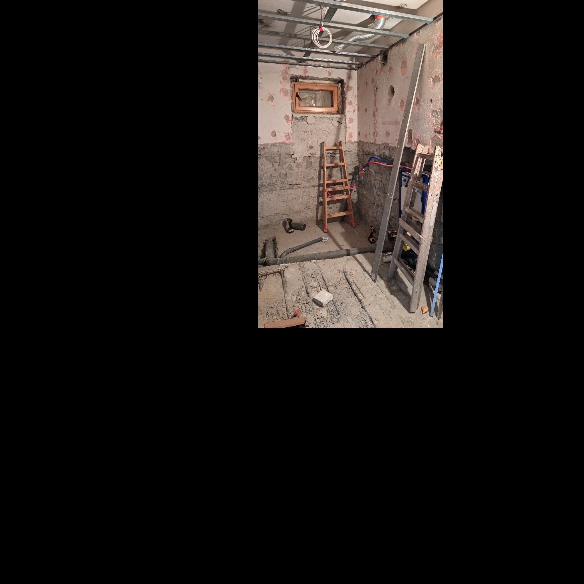 Wnętrze łazienki w trakcie remontu: odsłonięte rury, drabiny, surowy beton, przygotowywana instalacja pod płytki. Widoczne narzędzia pracy i elementy konstrukcyjne.