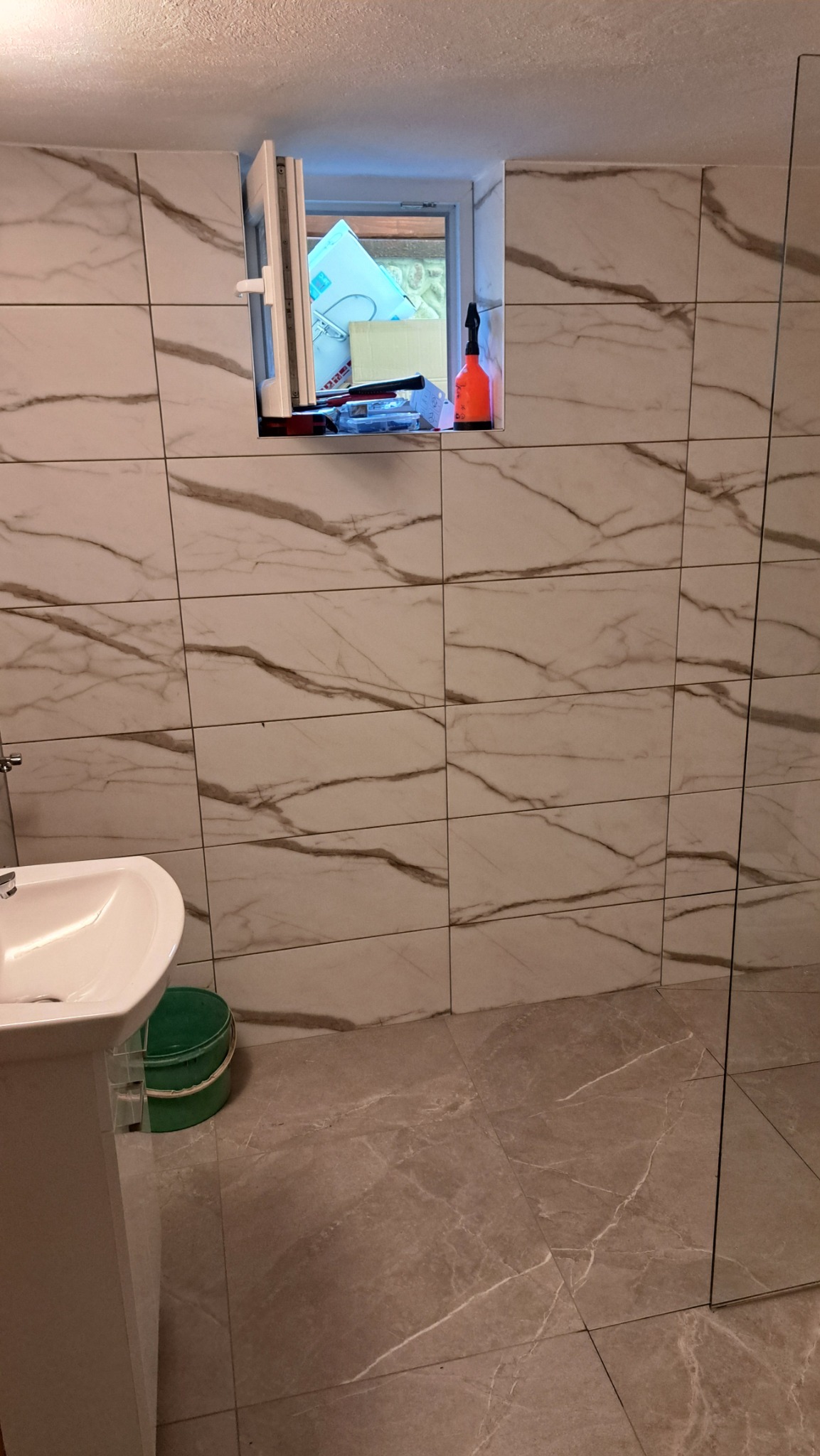 Wykończona łazienka z beżowymi płytkami imitującymi marmur na ścianach i podłodze. Widoczna umywalka na postumencie i kabina prysznicowa ze szkła.