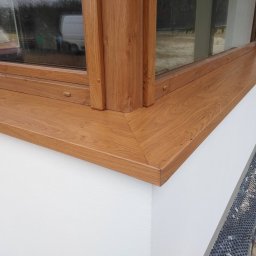 SolBud firma budowlana Krystian Solon - Fragment elewacji z zamontowanym oknem z drewnianą ramą i parapetem, widoczna warstwa ocieplenia przy gruncie.