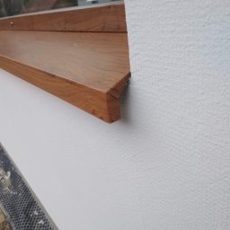 SolBud firma budowlana Krystian Solon - Nowy, drewnopodobny parapet zewnętrzny zamontowany na ocieplonej, białej elewacji budynku.