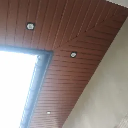 Podbitka dachowa z paneli PCV w kolorze brązowym, z wbudowanymi punktowymi lampami LED, widoczny fragment orynnowania i fragment ściany budynku.