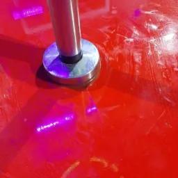 Błyszcząca, czerwona podłoga po nałożeniu gładzi, z widocznym metalowym elementem podtrzymującym pionową konstrukcję i smugami po szpachlowaniu.