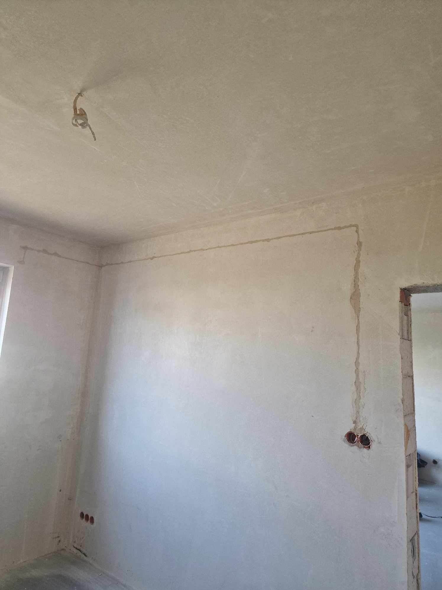 Surowe wnętrze w trakcie prac wykończeniowych: widoczne bruzdy pod kable elektryczne w ścianach i suficie, puszki instalacyjne bez osprzętu, wystające przewody z sufitu.
