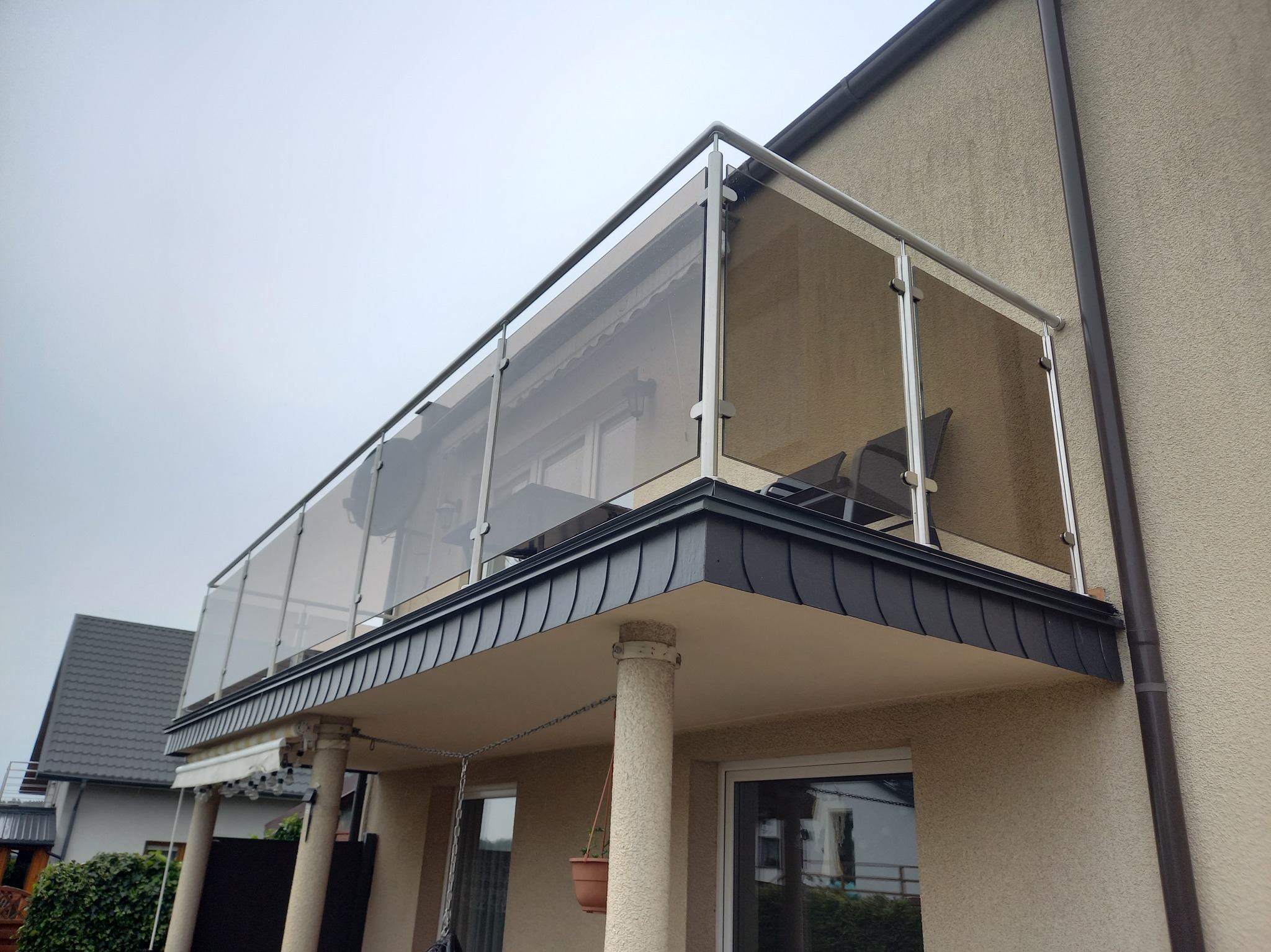 Szklana balustrada balkonowa z metalowymi słupkami, widok z dołu. Nowoczesny design, szare niebo w tle.