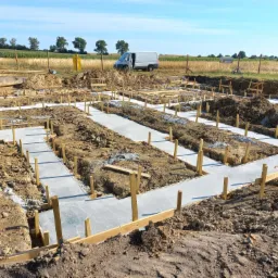 Wylane fundamenty pod dom jednorodzinny z drewnianym szalunkiem, widoczny samochód dostawczy w tle.