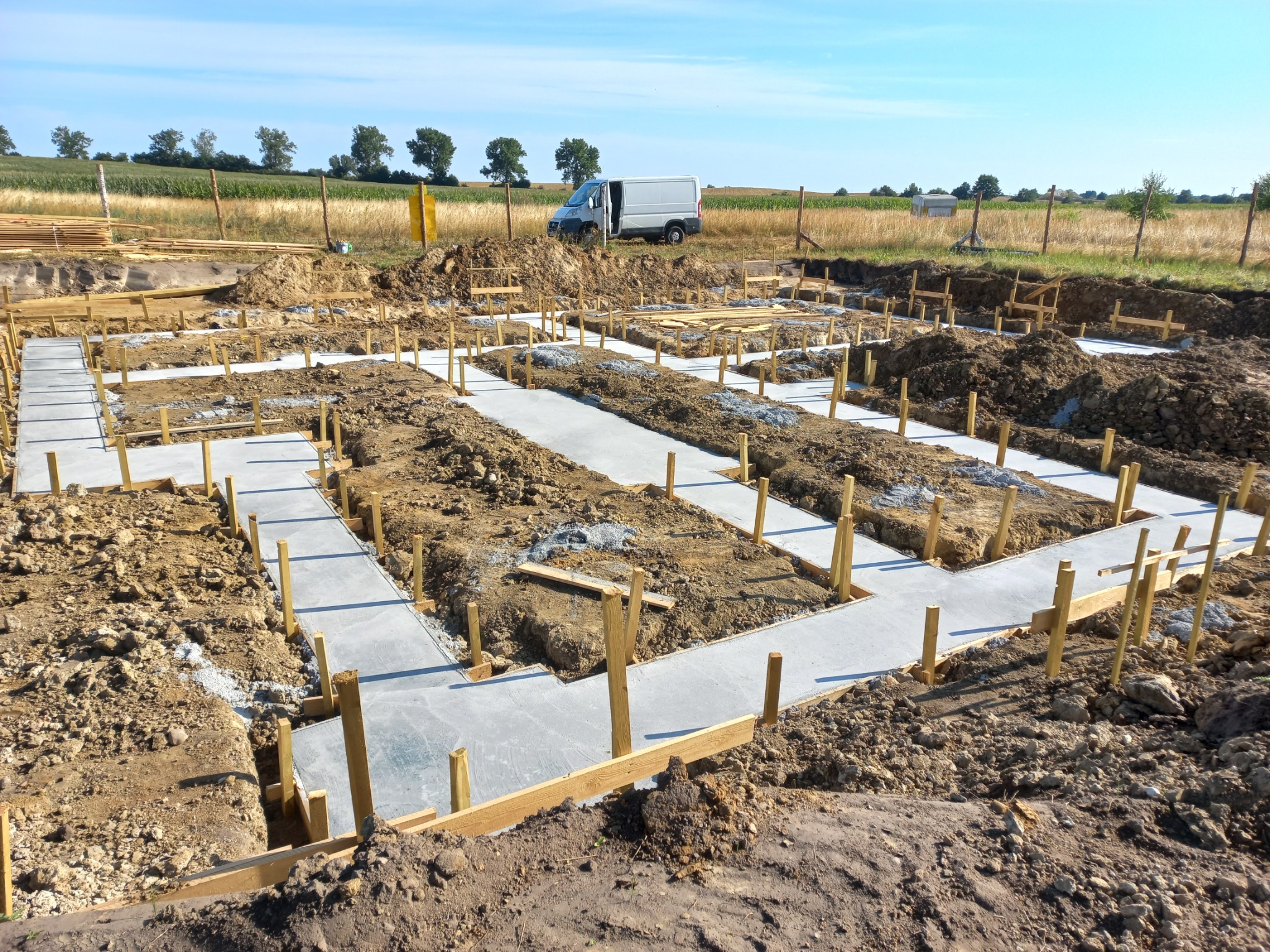 Wylane fundamenty pod dom jednorodzinny z drewnianym szalunkiem, widoczny samochód dostawczy w tle.