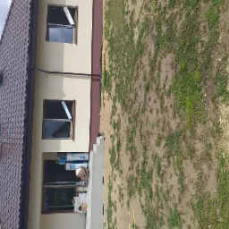 Fragment elewacji domu jednorodzinnego z widocznymi oknami w trakcie montażu, ociepleniem oraz stertą materiałów budowlanych przy wejściu.