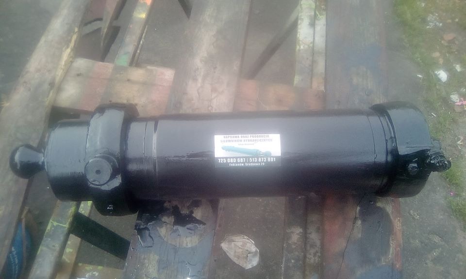 Czarny, odnowiony cylinder hydrauliczny z naklejoną etykietą producenta leżący na drewnianej palecie.