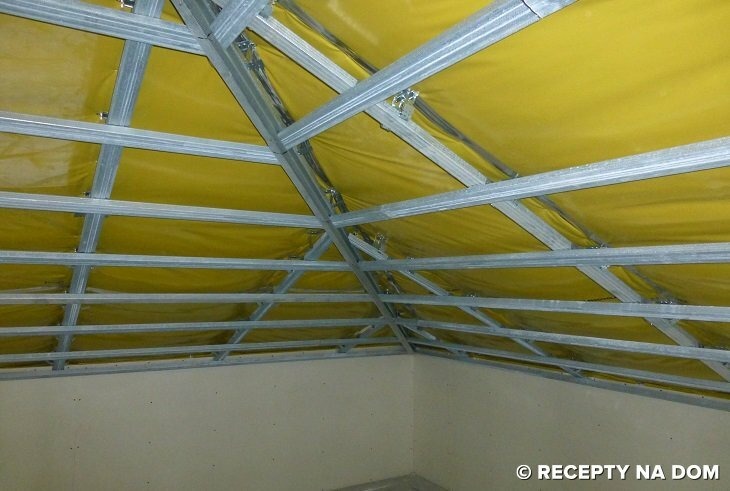 Konstrukcja szkieletowa poddasza z zamontowaną żółtą folią izolacyjną, widok od dołu na metalowe profile i mocowania.