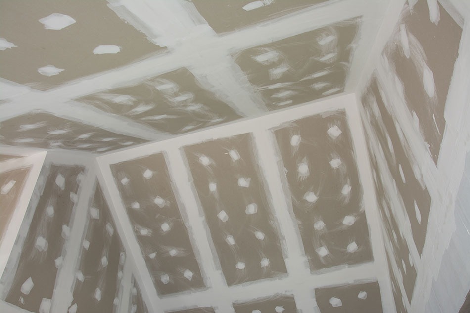 Wnętrze w trakcie przygotowania do malowania: ściany i sufit pokryte płytami gipsowo-kartonowymi z widocznymi łączeniami i zagipsowanymi otworami po wkrętach.