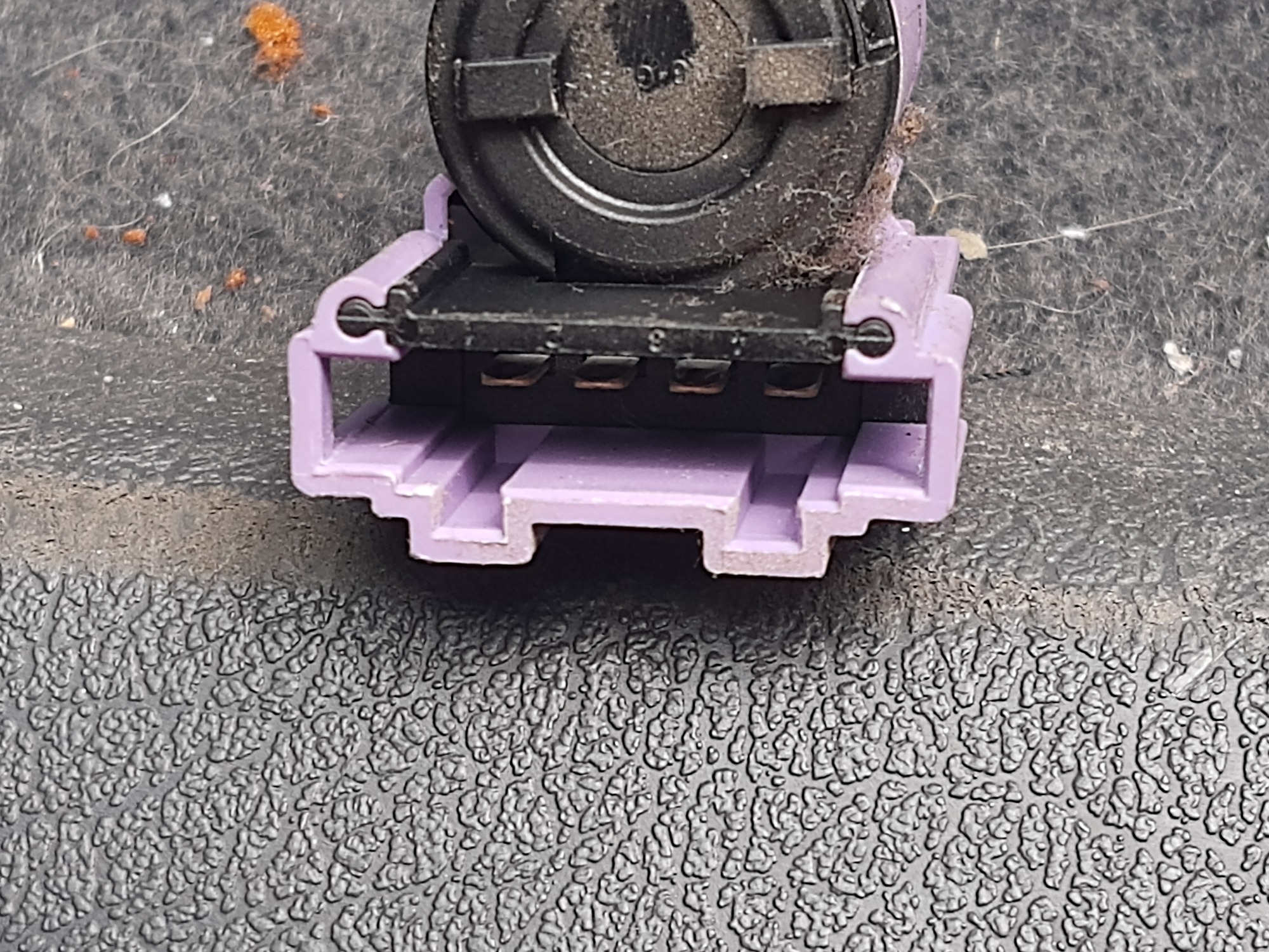 Zbliżenie na złącze elektryczne w odcieniach fioletu i czerni, widoczne metalowe piny, osadzone na teksturowanej, ciemnej powierzchni.