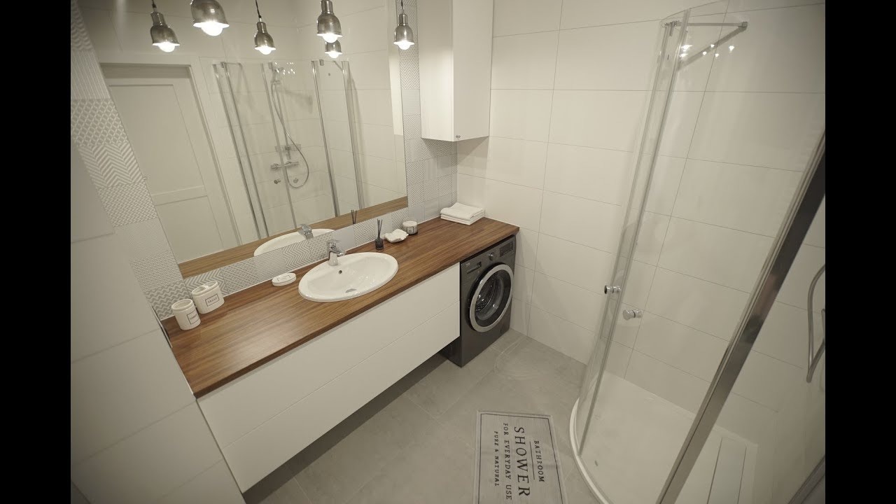Nowoczesna łazienka z prysznicem typu walk-in, umywalką nablatową na drewnianym blacie, pralką i dywanikiem z napisem 'SHOWER'.