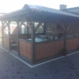 Zadaszona, drewniana altana z grillem murowanym w tle, otoczona brukowaną nawierzchnią.