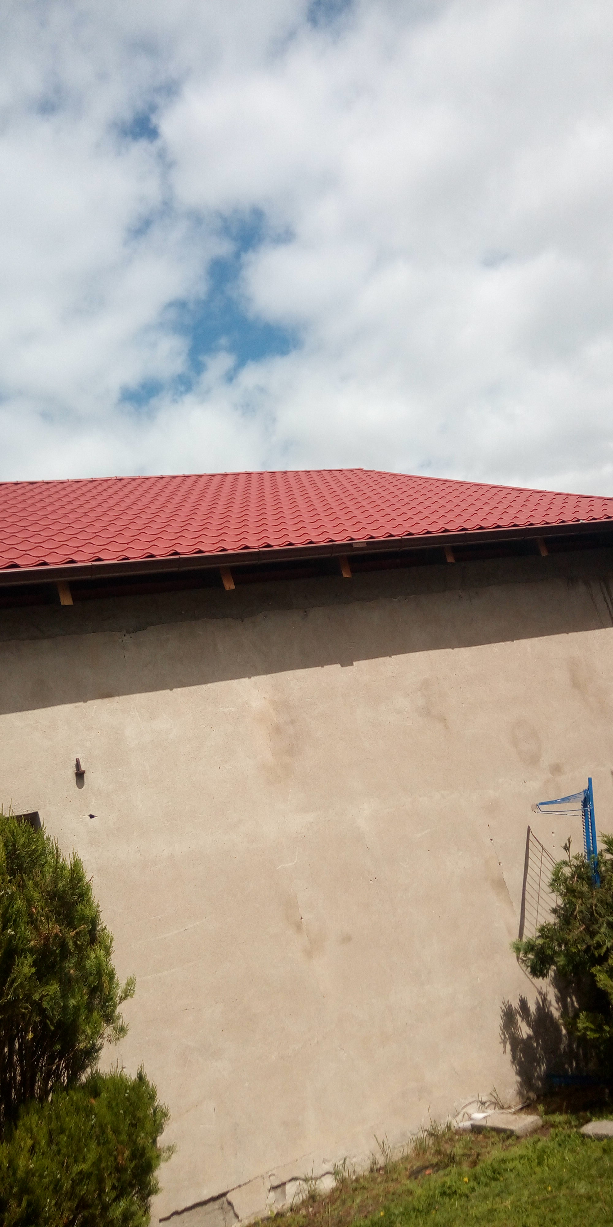 Czerwony dach z blachodachówki na budynku o beżowej elewacji, widok z dołu na tle pochmurnego nieba.