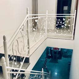 Errementari Adrian Leśniak - Biała, metalowa balustrada schodowa z motywem roślinnym, widok z góry na schody z szarego kamienia i fragment pomieszczenia z niebieską podłogą.
