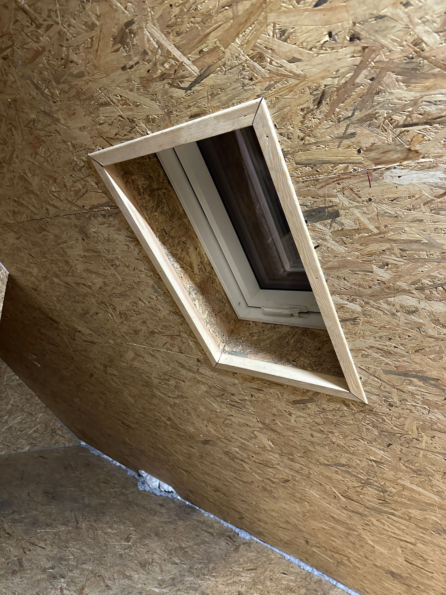 Okno dachowe w trakcie montażu w konstrukcji z płyty OSB, widoczna drewniana rama okienna i szczelina wypełniona pianką izolacyjną.