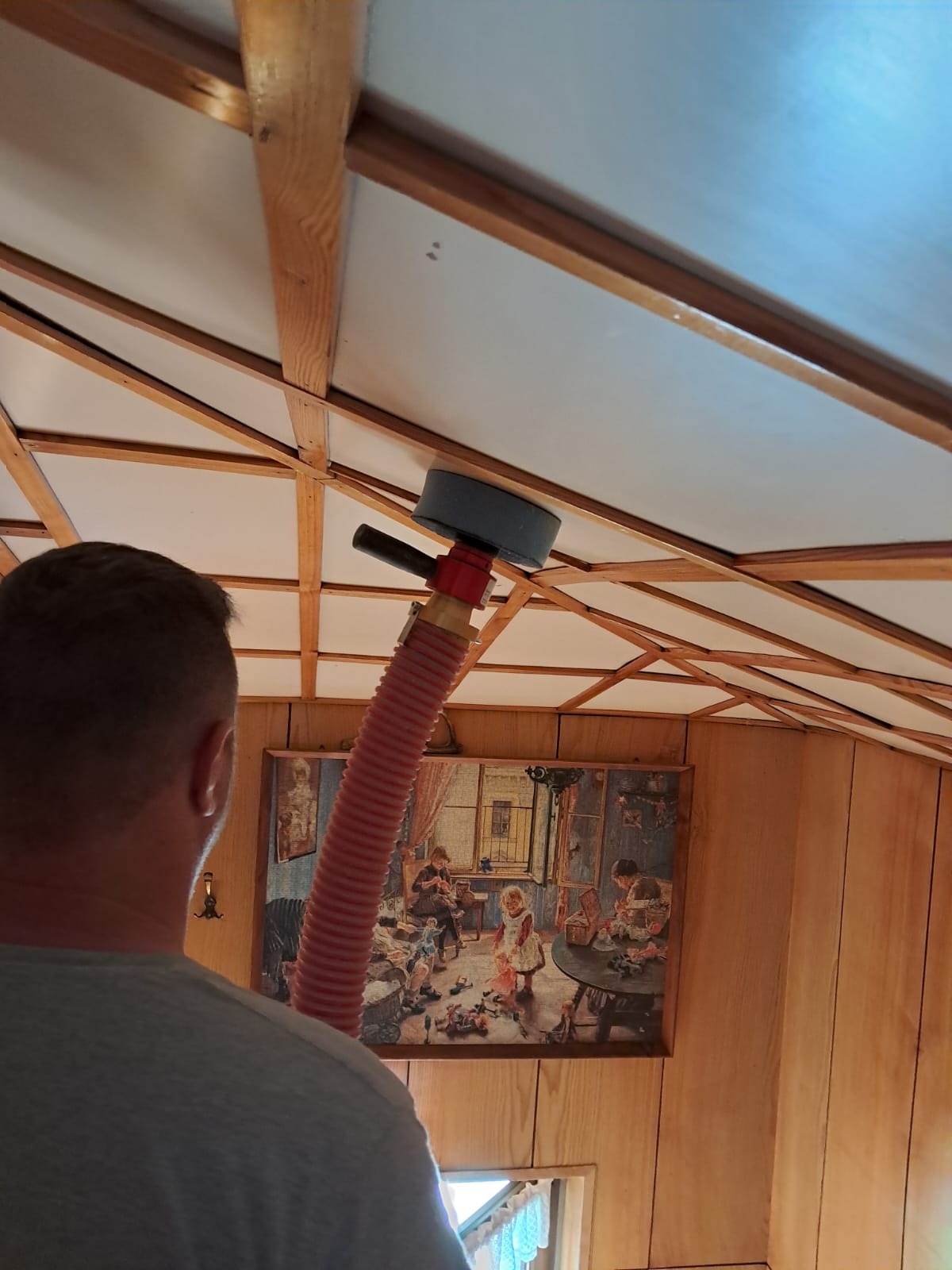 Aplikacja pianki PUR na poddaszu z drewnianą konstrukcją, widoczna czerwona rura aplikatora i obraz na ścianie w tle.