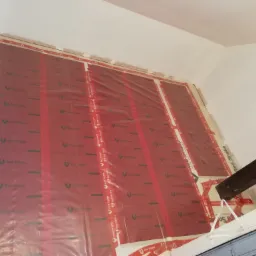 Ściana wewnętrzna w trakcie montażu izolacji termicznej z folią ochronną z nadrukiem 'Red Snake', widoczny fragment drewnianej belki stropowej.
