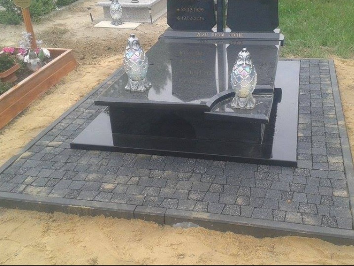 Ciemna kostka brukowa wokół czarnego nagrobka z dwoma lampionami w kształcie sowy na cmentarzu.