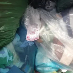 Wnętrze pojemnika lub kontenera wypełnionego workami z odzieżą, widoczna ulotka informacyjna dotycząca zbiórki odzieży z napisem 'LIDERSAMMLUNG DONNERSTAG ab 8 Uhr'.