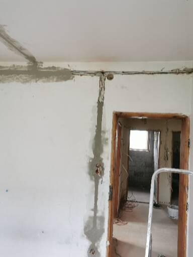 Wewnętrzna instalacja elektryczna w trakcie montażu: kable prowadzone po ścianie i suficie, zabezpieczone gipsem, widoczne puszki instalacyjne i fragment drabiny w tle.