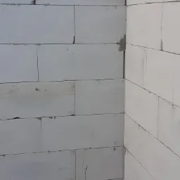 Fragment ściany domu z białych bloczków betonowych, widoczny narożnik, drobne ubytki w spoinach.