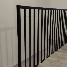 Czarna, metalowa barierka z pionowymi szczeblami na antresoli, widok na remontowane poddasze z suszarką na ubrania