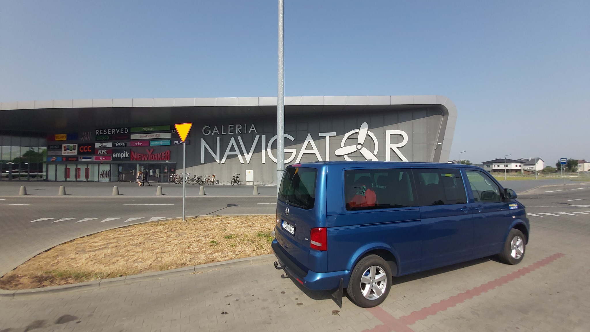 Niebieski van Volkswagen Transporter zaparkowany przed Galerią Navigator, widoczne tablice rejestracyjne, w tle sklepy Reserved, CCC, Empik i New Yorker.
