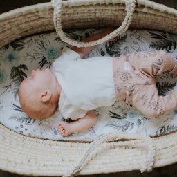Ulotne chwile- Filipiak fotografia - Śpiący noworodek w wiklinowym koszu Mojżesza na pościeli w kwiaty, ubrany w białe body i różowe spodenki w pandy.