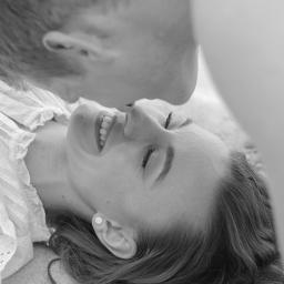 Ulotne chwile- Filipiak fotografia - Czarno-białe zbliżenie na uśmiechniętą kobietę leżącą na piasku, mężczyzna delikatnie dotyka jej nosa swoim.