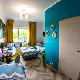 Pokoje Hotelowe Siedlczanka - Pokój z trzema łóżkami pojedynczymi, stolikiem z przekąskami i kwiatami, dekoracyjną tapetą z motywem zwierzęcym i turkusową ścianą z okrągłymi lustrami.