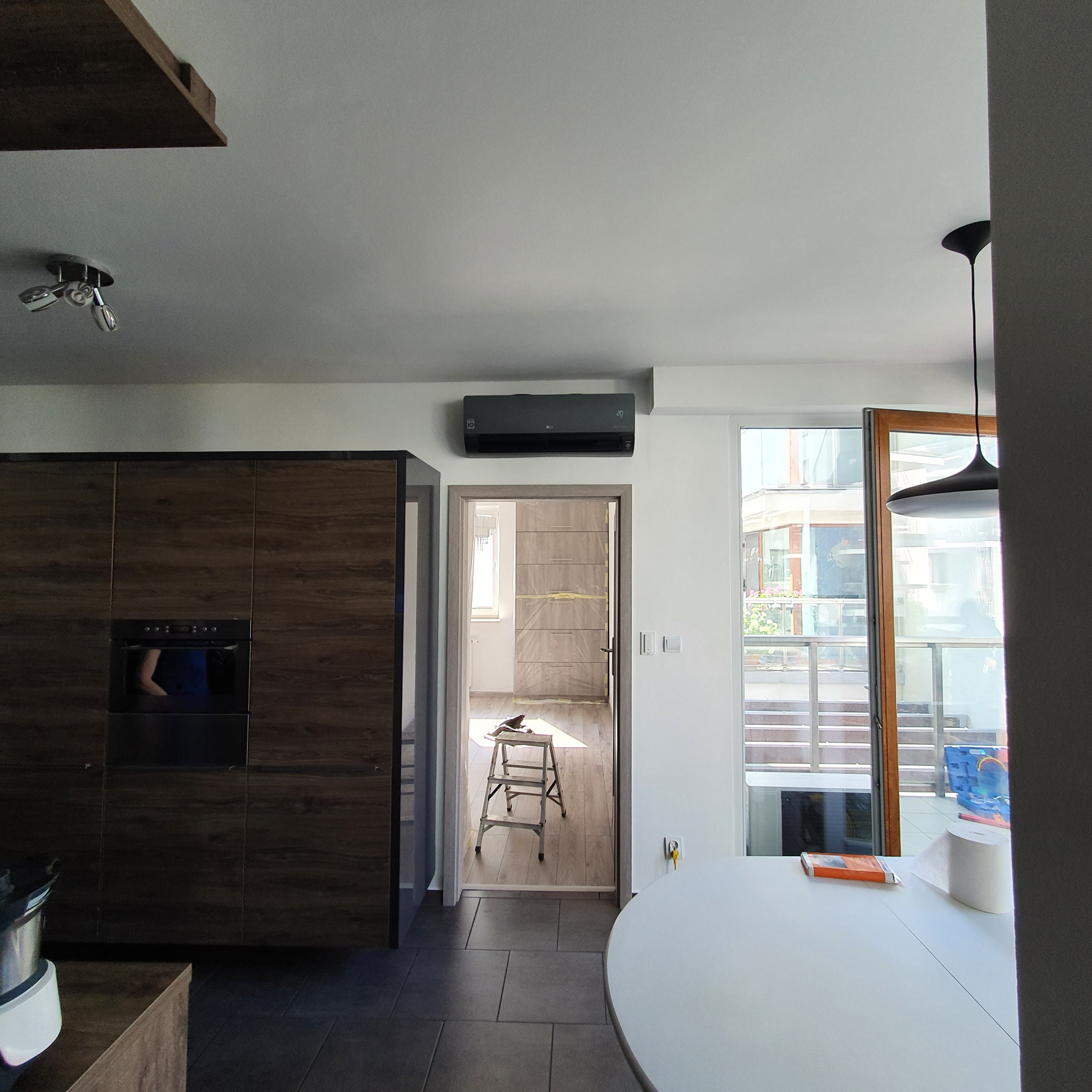 Czarny klimatyzator LG zamontowany nad drzwiami w nowoczesnym mieszkaniu, widoczna drabina w pokoju obok, sugerująca prace instalacyjne.