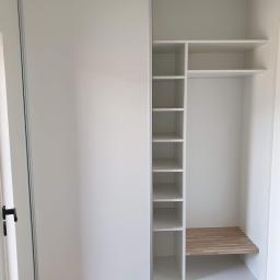 Expert Serwis bis sp z o o - Wnętrze białej szafy wnękowej z przesuwnymi drzwiami, widoczne półki i drewniana wstawka na dolnej półce, oświetlenie sufitowe żarówką.