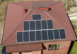 Widok z góry na dach domu z cegły z zainstalowanymi panelami słonecznymi ułożonymi w dwóch rzędach, z kominem na górze.