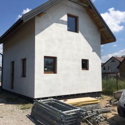 Krystian S. Docieplenia-remonty od A do Z - Surowa elewacja domu jednorodzinnego po szpachlowaniu w Końskich, widoczne rusztowania i przygotowane deski, w tle zabudowa jednorodzinna.