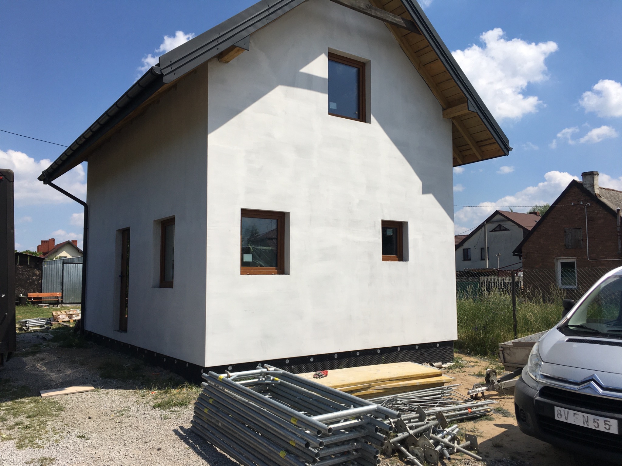 Surowa elewacja domu jednorodzinnego po szpachlowaniu w Końskich, widoczne rusztowania i przygotowane deski, w tle zabudowa jednorodzinna.