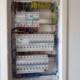 Rozdzielnica elektryczna z zamontowanymi bezpiecznikami, widoczne przewody w różnych kolorach, starannie ułożone wewnątrz obudowy.