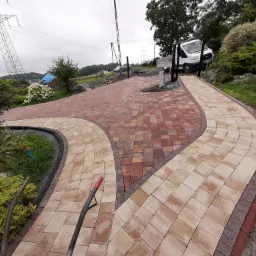 Rozwidlający się chodnik z kostki brukowej w dwóch odcieniach, z widocznym w tle samochodem dostawczym i słupami wysokiego napięcia.