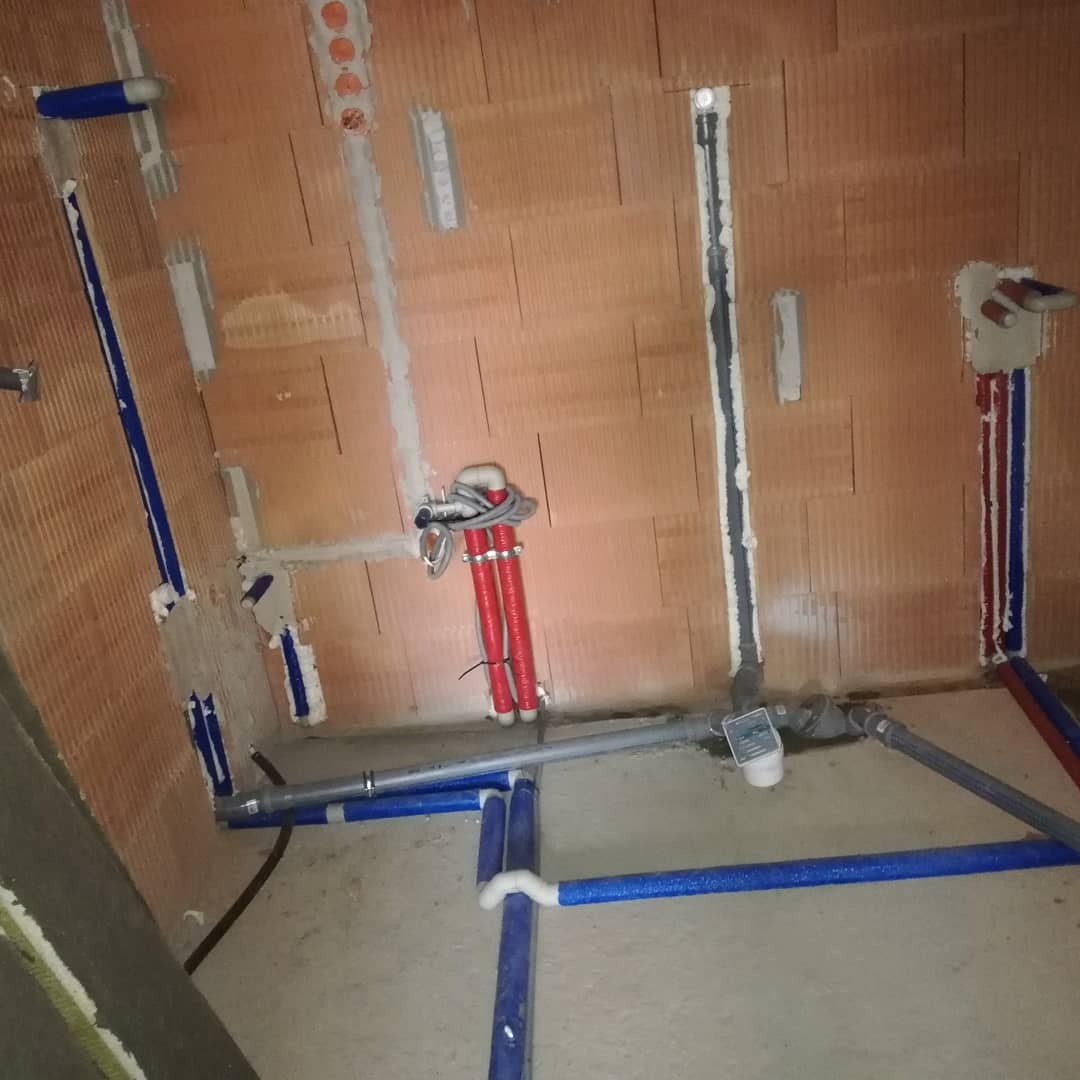 Montaż instalacji wodnej w surowym stanie: widoczne rury PEX w izolacji, kształtki, oraz fragmenty instalacji w ścianach z cegły dziurawki.