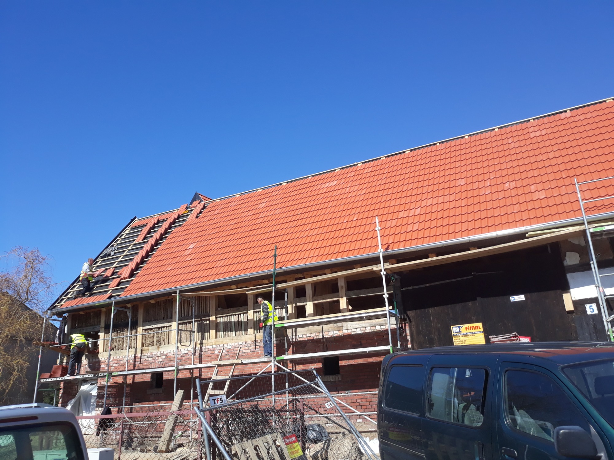 Prace dekarskie w Słupsku: ekipa montuje czerwoną dachówkę na konstrukcji więźby, widoczne rusztowania i częściowo ocieplona ściana budynku.