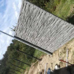 Pojedynczy panel ogrodzeniowy z betonu imitującego kamień, ustawiony pionowo podczas montażu, widoczna poziomica i fragment siatki ogrodzeniowej w tle.