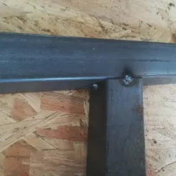 Detale spawania: Połączenie prostopadłe dwóch stalowych profili kwadratowych, widoczny spaw na tle płyty OSB.