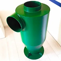 Zielony, metalowy cyklon odpylający, stojący na drewnianej podłodze, z widocznymi spawami i otworami wlotowymi, sfotografowany z góry pod kątem.