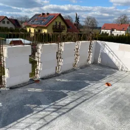 Wznoszone ściany z betonu komórkowego Ytong zbrojone stalą na betonowej płycie fundamentowej, widok z góry na budowę domu jednorodzinnego w słoneczny dzień.