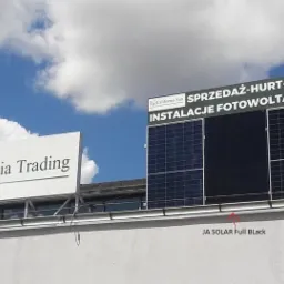 Instalacja paneli słonecznych JA Solar Full Black na dachu budynku z reklamami firm California Trading i California Sun oferujących sprzedaż hurtową i detaliczną oraz instalacje.